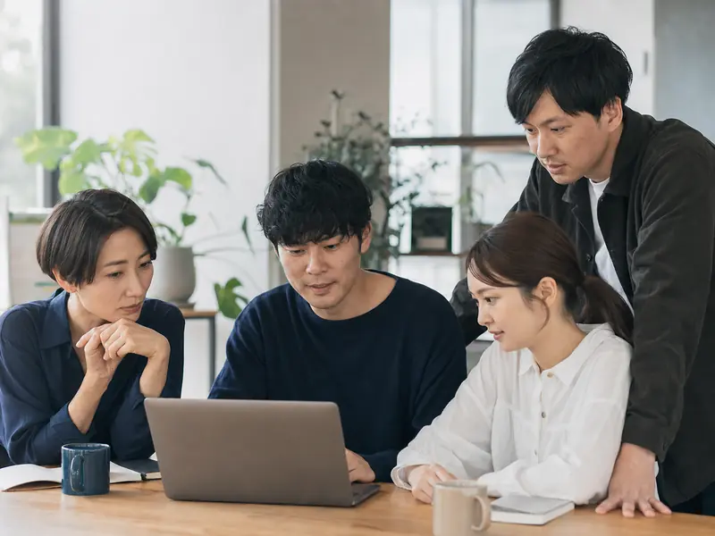 オフィスでノートパソコンを囲み業務改善を話し合うチーム